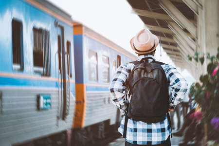 African male traveler with hat and backpack waiting for the train on railway station.Adventure travel conceptの写真素材