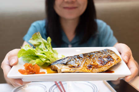 Asian woman holding a plate with grilled saba fish steak with teriyaki sauce in the Japanese food restaurantの写真素材