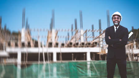 African site contractor engineer with hard hat holding blue print paper with building in backgroundの写真素材