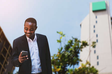 African businessman wears a black suit and uses a stylish smartphone with smile and happyの写真素材