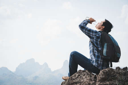 Success man hiker drink water at cliff edge on mountain top. Concept of traveling and hiking adventuresの写真素材