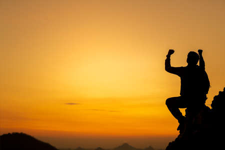 Silhouette of success man hiker outstretched arms on top of the mountain with beautiful sunset....