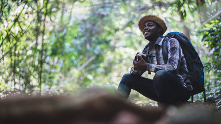 Smile charming African traveler with backpack and film camera is happily resting at the national park. Concept of Adventure travel and  vacations going hikingの写真素材