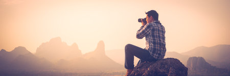 Nature photographer traveler taking photo of beautiful landscape from top of the mountain.Concept of adventure travel, mountaineering and photographyの写真素材