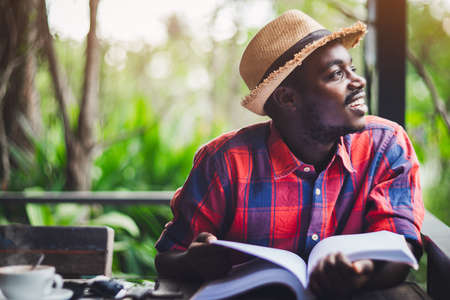 African traveler in a hat with a book and a cup of coffee thinking and looking outside to the view