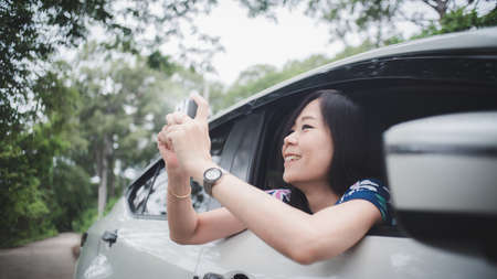 Happy asian woman taking photo and looking out of car with smile and relax.Concept of travel and transportationの写真素材