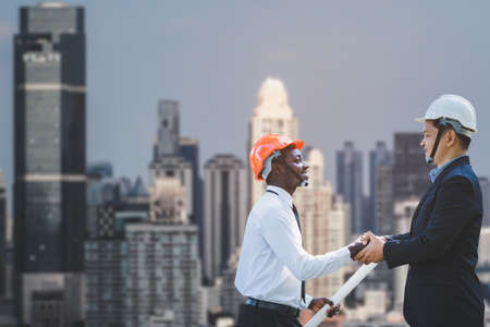 Smiling african engineer and asian construction managers shaking hands at construction site with the...