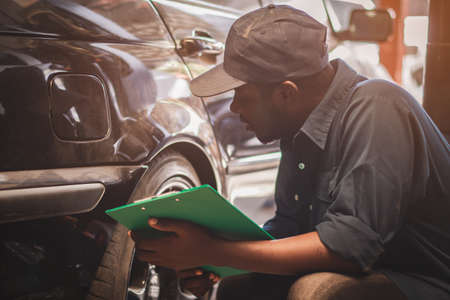 African maintenance male checking car with use wrench and tablet , service via insurance system at Auomobile repair and check up centerの写真素材