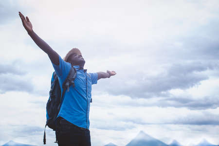 African traveler man with backpack enjoying the view in nature.Freedom man standing with arms outstretched on blue sky white cloud summer landscape dayの写真素材