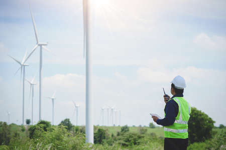 Engineer man stand holding tablet front the wind turbines generating electricity power station. Concept of sustainability development by alternative energyの写真素材