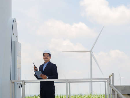 Asian engineer manager in a suit is using a tablet to control and monitor the operation of a wind turbine in the electrical control room.Concept of sustainability development by alternative energyの写真素材