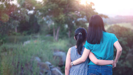 Mother and daughter are hugging and looking outdoor in green nature with sunset.Concept of mother's dayの写真素材