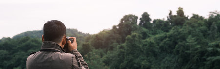 The photographer with jacket taking photo by a camera in a mountains. Creative professional...
