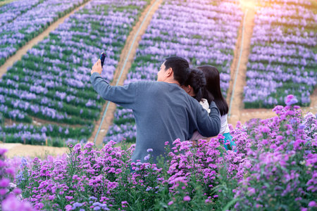 Happy family holding smart phone selfie photo at floral flowers park with beautiful landscape nature backgroundの写真素材