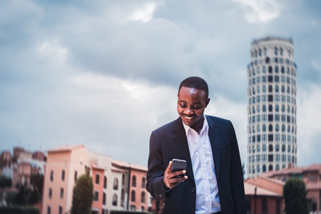 African businessman holding smartphone with wearing suit outside residential property in city townの写真素材