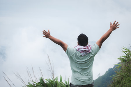 A mountaineer climber stands with his arms outstretched to convey success and freedom atop a misty...
