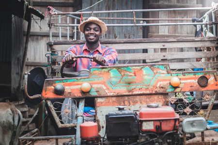 African smiling man farmer driving old vintage tractor with trailer on farm.Concept of agriculture and cultivationの写真素材