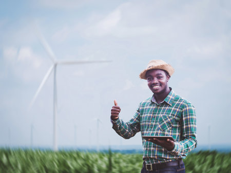 African farmer standing and holding digital tablet on corn farm with  wind turbine in background.Concept of green power sustainability resources  development by alternative energyの写真素材