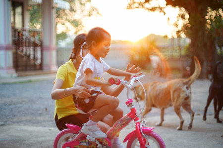 Asian mother teaches and trains her daughter to ride her first bike at sunsetの写真素材