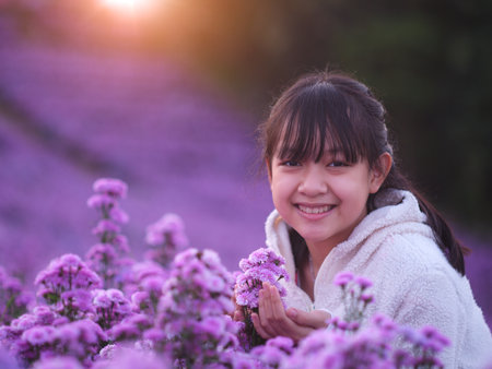 A brightly smiling little girl in white coat stands in a field of margarets flowersの写真素材