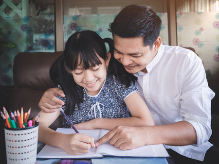 Father is teaching his daughter's homework happily and full of smiles.Concept of Father's Dayの写真素材