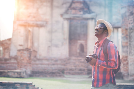 Young man traveler with backpack and hat standing in front of ancient temple.の写真素材