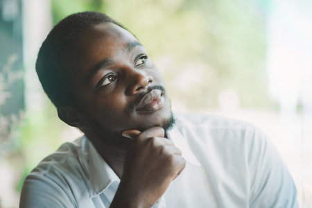 African businessman in white shirt looking out the window, thinking about workplace business problems.Black man sits and thinks for inspiration to find a solution to problems in lifeの写真素材