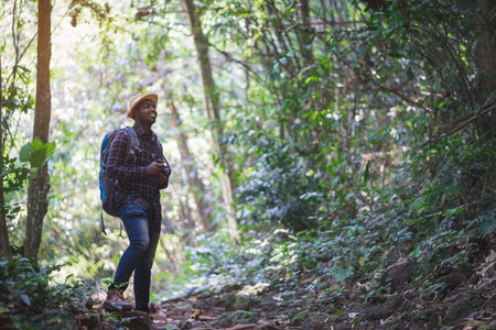 Smile charming African traveler with backpack and film camera is happily resting at the national park. Concept of Adventure travel and  vacations going hikingの写真素材