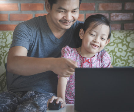 A father teaches his daughter how to use a computer to study online and search the internetの写真素材