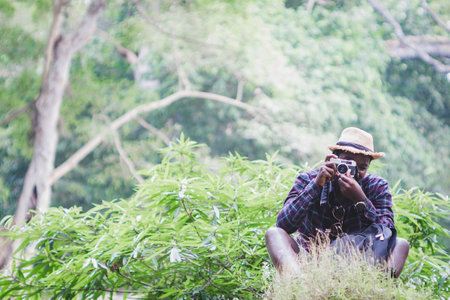 Charming African hiker is happily resting at the national park with backpack and camera. Concept of Adventure travel and Photographyの写真素材