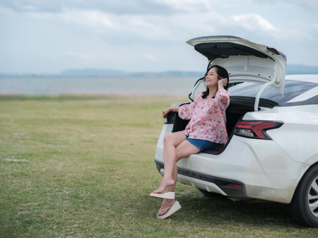 Asian woman sitting in the trunk of a car during a holiday travel trip.Traveling car conceptの写真素材