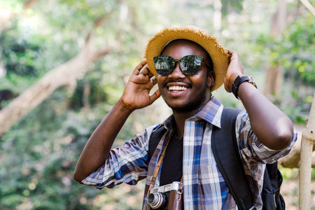 Charming African hiker is happily resting at the national park with backpack and camera. Concept of Adventure travelの写真素材