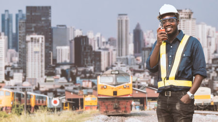 African mechanical engineer talking with radio communication or walkie talkie to maintain train in city center with tall buildings in the backgroundの写真素材