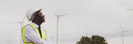 African engineer stand with smile near the wind turbine for inspect the operation of large wind turbines that converts wind energy into electrical energyの写真素材