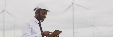 African engineer smile and using tablet with the wind turbine for inspect the operation of large wind turbines that converts wind energy into electrical energyの写真素材