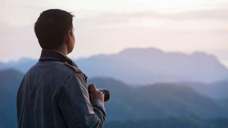The photographer with jacket taking photo by a camera in a mountains. Creative professional photographing.Travel, hobby and active lifestyle conceptの写真素材