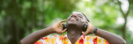 African man in casual clothes sitting happily listening to music on his mobile phone using...