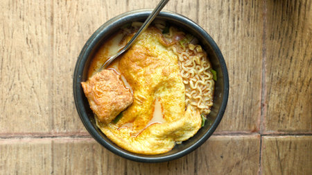 Noodle soup with egg in black bowl on wooden tableの写真素材