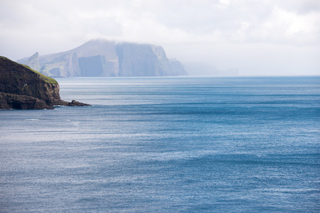 Typical landscape on the Faroe Islands as seen from Mykines with blue ocean and cloudsの写真素材