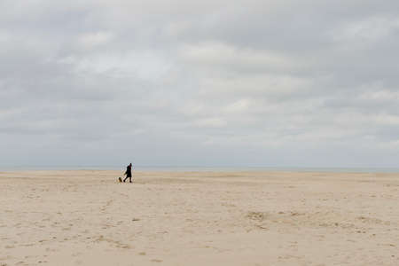 Oostduinkerke, Belgium - November 16, 2019: A woman walks her dog on the beach on a cold November dayのeditorial素材