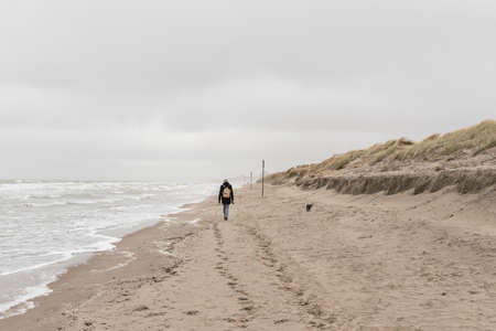 Koksijde,Belgium - February 26, 2020: Woman walking on the beach on a a cold and windy dayのeditorial素材