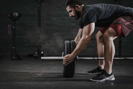 Young crossfit athlete preparing barbell for lifting weight at the gym. Magnesia protection dust cloud. Handsome man doing functional training. Practicing powerlifting. Workout exercises.の写真素材