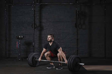 Young crossfit athlete doing deadlift exercise with heavy barbell at the gym. Man practicing functional training powerlifting workoutの写真素材