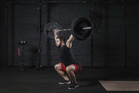 Young cross fit athlete doing squats with barbell over head. Man practicing functional training. Powerlifting workout exercisesの写真素材