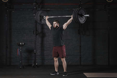 Young athlete lifting barbell overhead at the crossfit gym. Handsome man doing functional training. Practicing powerlifting. Workout exercisesの写真素材