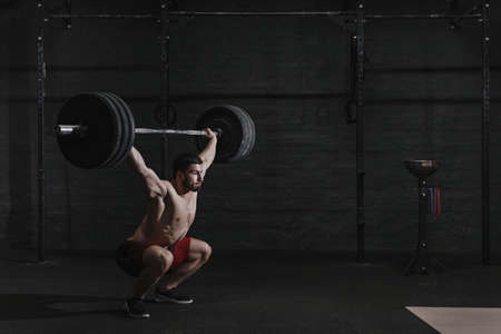 Young crossfit athlete lifting barbell overhead at the gym. Copy spaceの写真素材