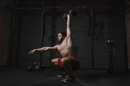 Crossfit athlete exercising at the gym doing overhead dumbbell squats.の写真素材