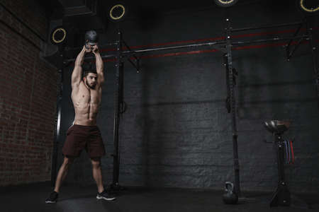 Athlete doing kettlebells swing exercise at crossfit gym. Handsome man doing functional training practicing workout. Copy space.の写真素材