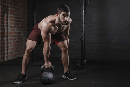 Crossfit athlete exercising with a kettlebell at the gym. Muscular man doing functional training practicing workoutの写真素材