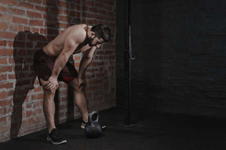 Athlete is leaning against the wall at the gym suffering breakdown to overcome. Demotivation sport concept. Stress and fatigue in sport. Crossfit kettlebell training. Copy space.の写真素材